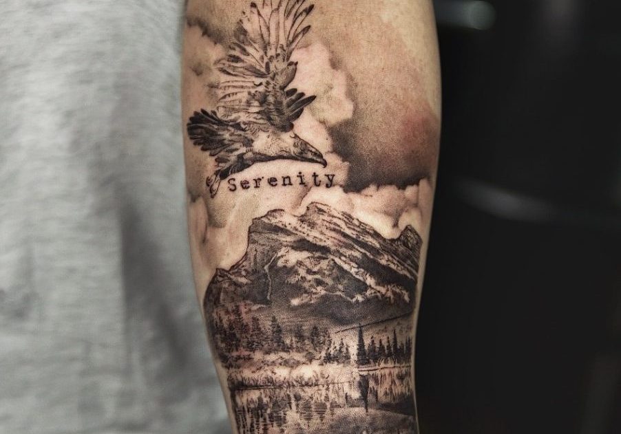 tattoo of landscape with a eagle soaring at the top with the word 'serenity' landscape has trees, mountains and water reflection